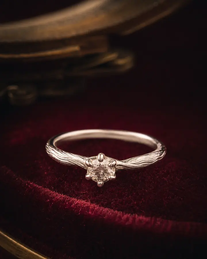 Cincin tunangan perak dengan batu kecil di atas kain maroon